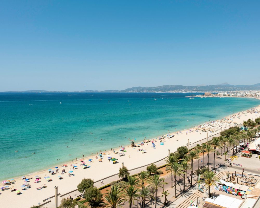 Vista panorâmica da Praia de Palma de Maiorca, com águas cristalinas e areia dourada, rodeada de restaurantes e hotéis perto da capital.